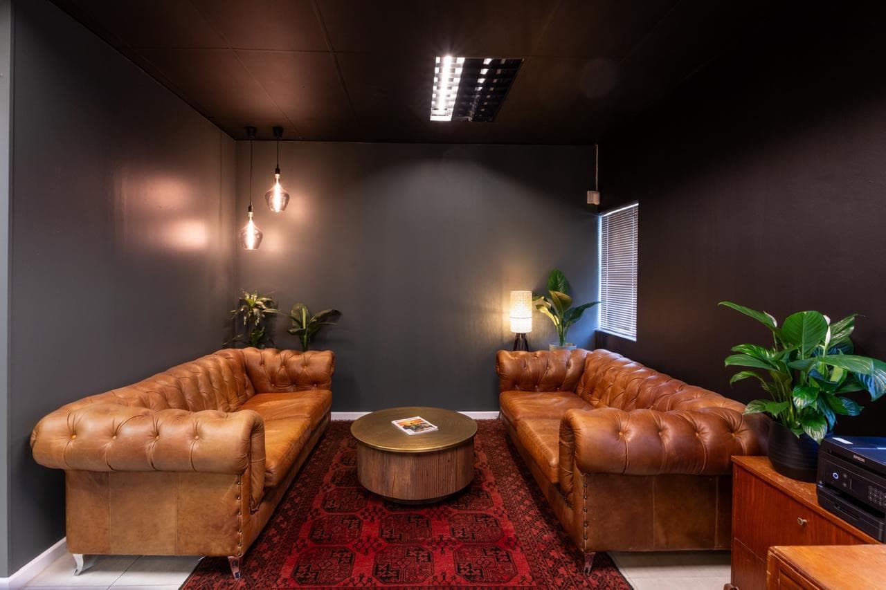 Two tan leather Chesterfields facing each other across a deep red Persian rug, lit by low amber pendants in the Blunt Box lounge