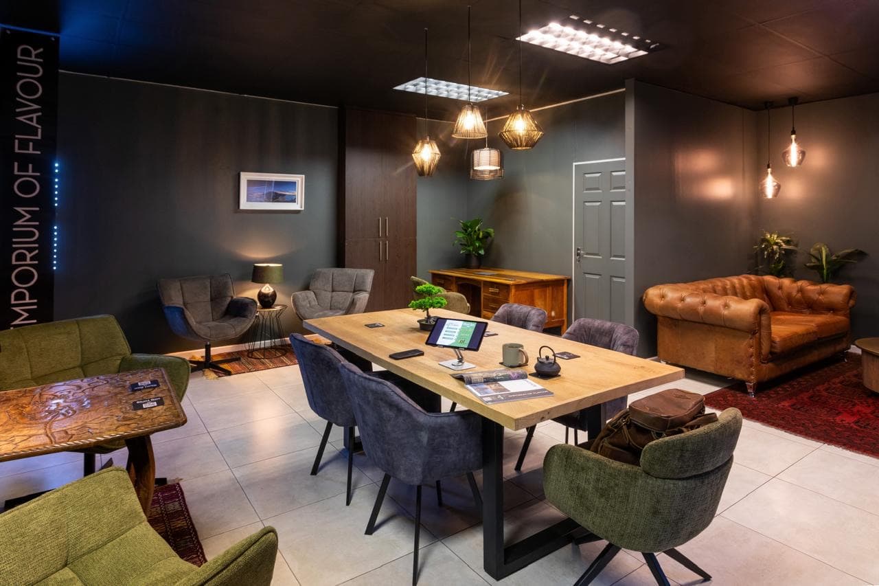 The members' lounge from the doorway: a long oak table, velvet chairs, woven pendant lights, and a tall banner reading Emporium of Flavour